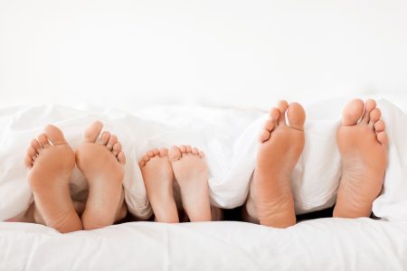 people, family and morning concept - bare soles or feet of parents and child in bed at home